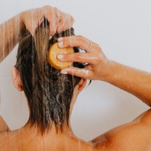 Back view of a woman washing her hair in the shower under running water.