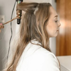 Profile of a woman having her hair curled with an iron in a salon setting.